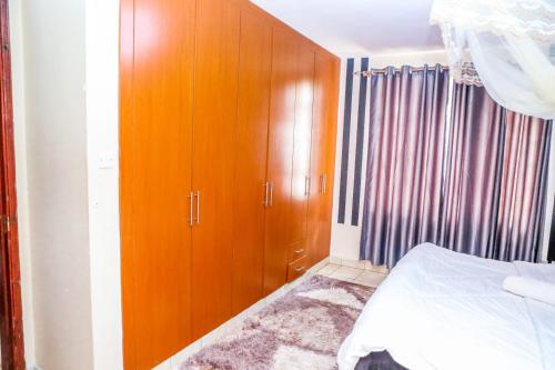 1 dormitorio con 1 cama y armario de madera en Genesis Executive mlimani en Kisumu