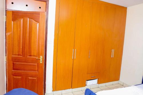 Habitación con armarios de madera, cama y puerta. en Genesis Executive mlimani en Kisumu