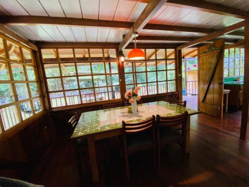 ein Esszimmer mit einem Tisch, Stühlen und Fenstern in der Unterkunft Wooden House Mindo - Casa de Las Nevadas in Mindo