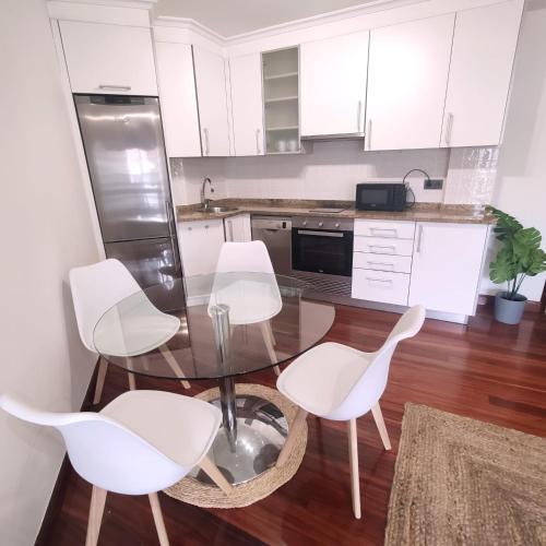 een keuken met een glazen tafel en vier witte stoelen bij Espectacular Apartamento Olívico con Parking in Vigo
