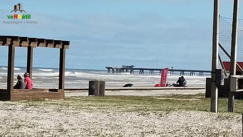 a group of people sitting on the beach near the ocean at 200m da Praia II 1,8km Congresso Est Catolica 2025 II Wi-Fi l 4 Pessoas l Churrasqueira l Elevador 3º Andar l Cadeira de Praia e Guarda Sol l Vaga Garagem in Tramandaí