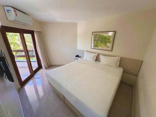 a bedroom with a large white bed and a window at Flat no hotel jatiúca suítes in Maceió