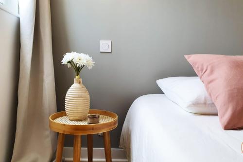 un vase avec des fleurs sur une table à côté d'un lit dans l'établissement Le Petit Biscuit - Centre Historique du Havre, au Havre