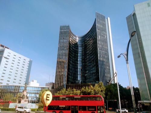 a red double decker bus in front of a tall building at Beautiful Apartment Reforma77 22thfloor 1bdr 2bath in Mexico City