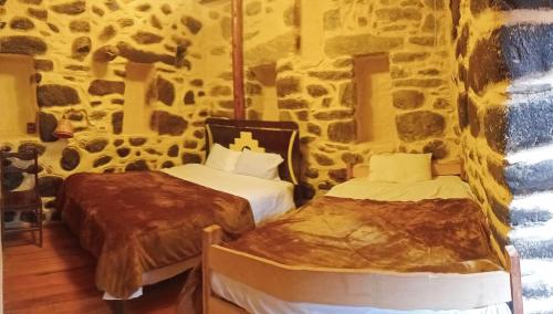 two beds in a room with a stone wall at Punto Sagrado in Ollantaytambo