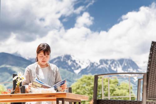 een vrouw die aan een tafel zit een boek te lezen met bergen op de achtergrond bij グランコテージ白馬 in Hakuba
