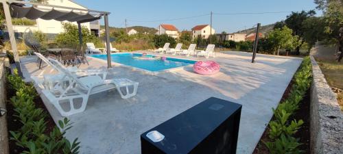 einen Pool mit weißen Stühlen und einem rosa Ball in der Unterkunft Family friendly apartments with a swimming pool Vinisce, Trogir - 12676 in Vinišće