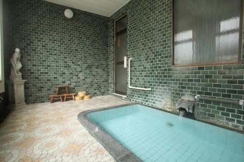 baño con bañera grande con pared de ladrillo en Tsukasaya Ryokan, en Tsuruoka