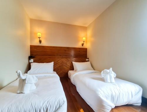 two beds in a room with white sheets and towels at The Peace River Kwai in Ban Tha Makham