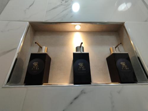 three black soap dispensers on a shelf in a bathroom at Zamá Room Hotel in Medellín