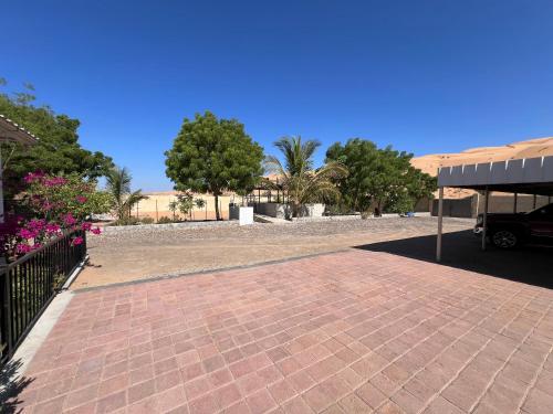 a brick parking lot with trees and a building at Big dune camp in Ḩawīyah