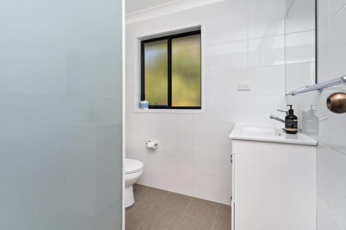 a white bathroom with a toilet and a window at Ammaboolah at Hat Head - 36 Hutcheson Street in Hat Head