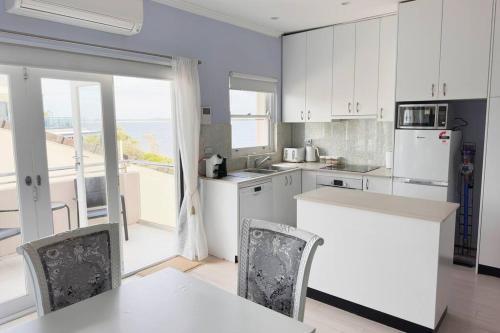 een keuken met witte kasten en een tafel en stoelen bij Sunny Apt on The Esplanade - Aircon in Cronulla