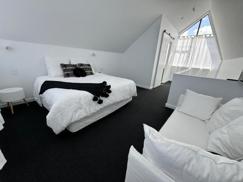 a white bedroom with a black cat laying on a bed at Matakana Luxury Escapes in Matakana