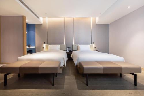 two beds in a hotel room with two benches at Atour Hotel Xiamen Jimei Lake Business Center in Xiamen