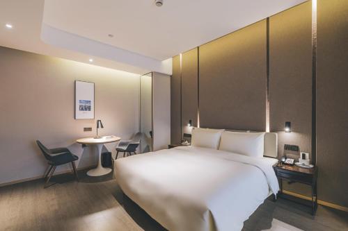 上海市にあるAtour Hotel North Bund Shanghaiの白い大型ベッドとテーブルが備わるホテルルームです。