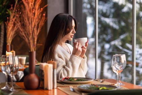a woman sitting at a table with a cup of coffee at Stara Pravda Hotel in Bukovel