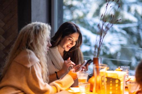 two women sitting at a table looking at a cell phone at Stara Pravda Hotel in Bukovel