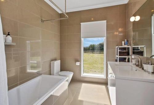 a bathroom with a tub and a toilet and a window at The Source, Otways in Tanybryn