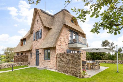 an old house with a thatched roof with a table and an umbrella at Fien to Huus in Wenningstedt