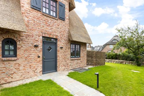 a brick house with a blue door and a yard at Fien to Huus in Wenningstedt