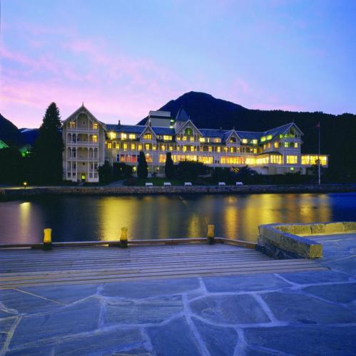 a large building sitting on the water at night at Kviknes Hotel in Balestrand