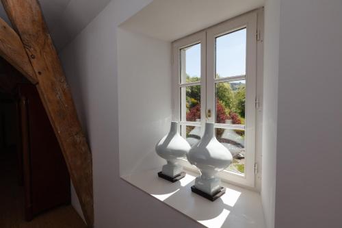 dwie białe wazy siedzące na półce obok okna w obiekcie L'annexe du Moulin Renaudiots w mieście Autun