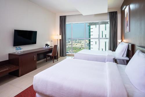 シャルジャにあるFour Points by Sheraton Sharjahのベッド2台、デスク、テレビが備わるホテルルームです。