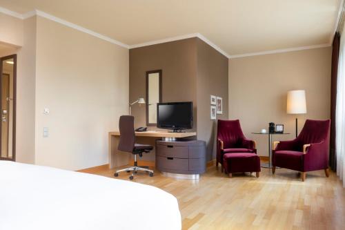 a room with two chairs and a desk with a television at Hilton Mainz in Mainz