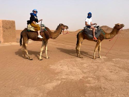 two people riding on camels in the desert at Mhamid yaya camp in Mhamid