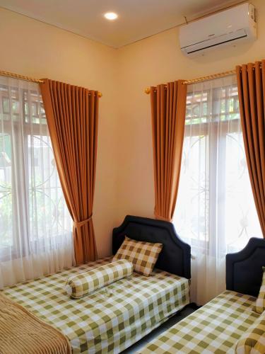 a bedroom with two beds and windows with curtains at Penginapan Prambanan TRISAN in Randugunting