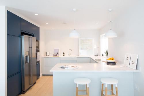 a white kitchen with a large white counter and stools at Insta-worthy 4br designer house 5 min to the beach in West Wittering