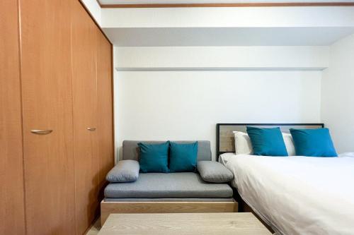 a bedroom with a bed and a couch with blue pillows at Alita Mansion Kyobashi in Osaka