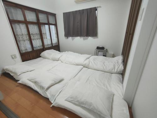 ein Bett mit weißer Bettwäsche und ein Fenster in einem Zimmer in der Unterkunft 佐世保　貸切小さな一軒家　GUEST HOUSE　楽楽 Luck-Luck in Sasebo