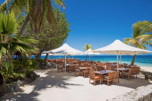 a restaurant on the beach with tables and umbrellas at Castaway Island, Fiji in Castaway Island