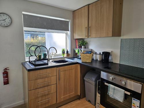 a kitchen with wooden cabinets and a sink and a window at Pet Friendly 2 Bed Coastal Property - Millendreath, Looe in Looe