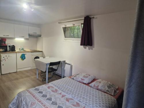 a bedroom with a bed and a table and a kitchen at Studio à Orsay à 5 min du RER B Le Guichet in Orsay
