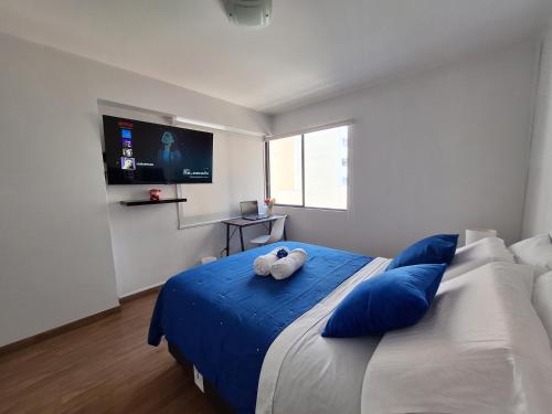 Habitacion baño Propio La Paz 1 في ليما: غرفة نوم مع سرير ووسائد زرقاء وتلفزيون