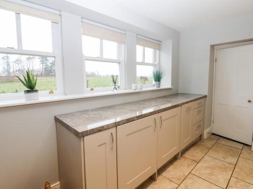 a kitchen with white cabinets and windows at Ravenside in Hexham