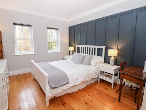 a bedroom with a white bed and a desk and two windows at Ravenside in Hexham