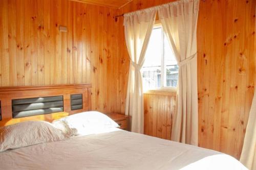 Schlafzimmer mit einem Bett mit Holzwänden und einem Fenster in der Unterkunft CABAÑAS LAS DALIAS ANCUD in Ancud