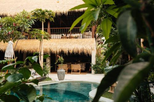 un complexe avec une piscine et un bâtiment au toit de chaume dans l'établissement Hani Hideaway, à Gili Air