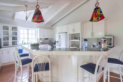 uma cozinha com armários brancos e uma grande ilha com cadeiras em Aura Dominica em Roseau