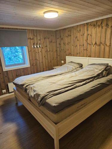 ein Bett in einem Schlafzimmer mit Holzwänden und einem Fenster in der Unterkunft Hytte i Ringsaker (Ljøsheim/Sjusjøen) in Ringsaker
