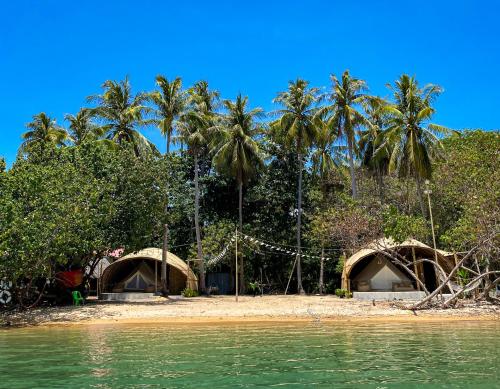 a beach with two huts and palm trees and the water at The Por Beach in Ko Por