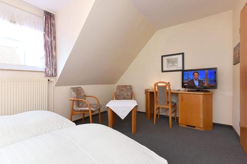 a bedroom with a bed and a desk with a television at Hotel Poggenstool in Neuharlingersiel