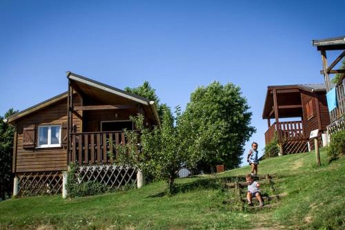dos niños jugando frente a una cabaña de madera en Camping Domaine Vallée du Tarn SN en Saint-Cirgue