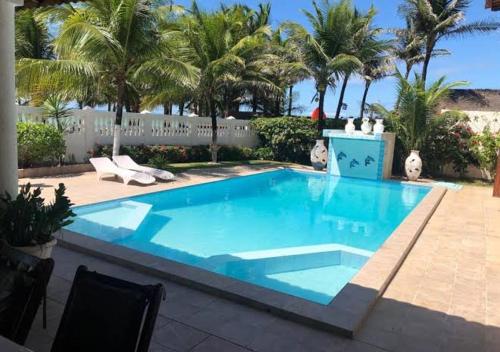 a blue swimming pool with palm trees and a fence at Casa de praia in Caucaia