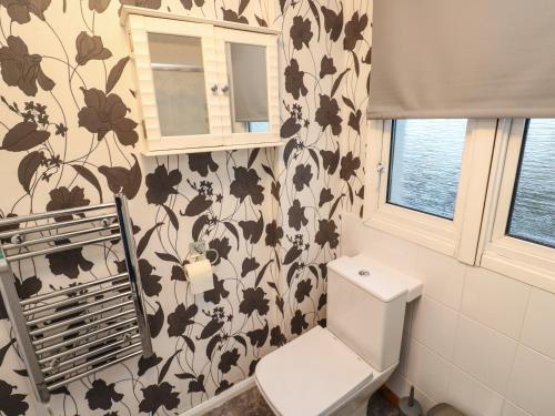 uma casa de banho com um WC e um papel de parede florido em Lamorna em Helston