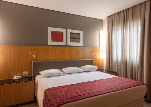 a bedroom with a large bed with a red blanket at DELPLAZA Marabá São Paulo in Sao Paulo